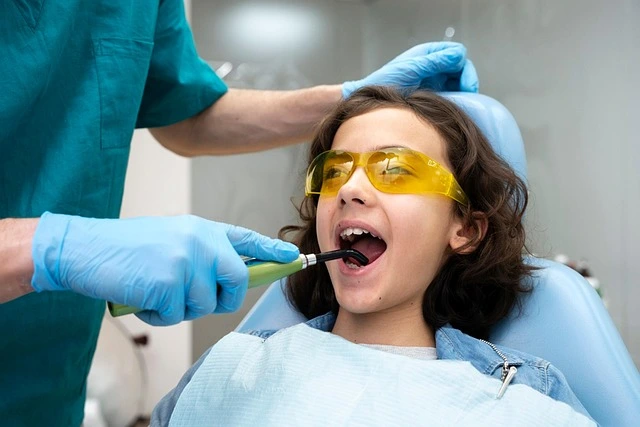 A photo of a child wearing protective glasses while a pediatric dentist gently examines their teeth during a routine dental visit.