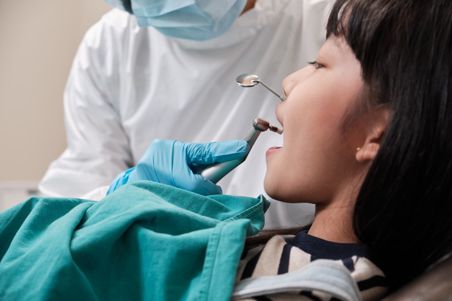Asian female pediatric dentist checks and examines a little Thai girl's caries teeth in dental clinic