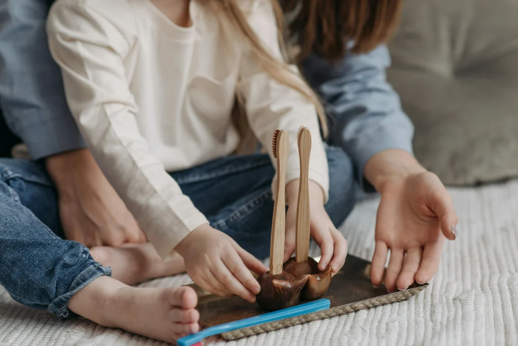 A photo of a child and parent holding toothbrushes during a playful toothbrushing routine on the floor.