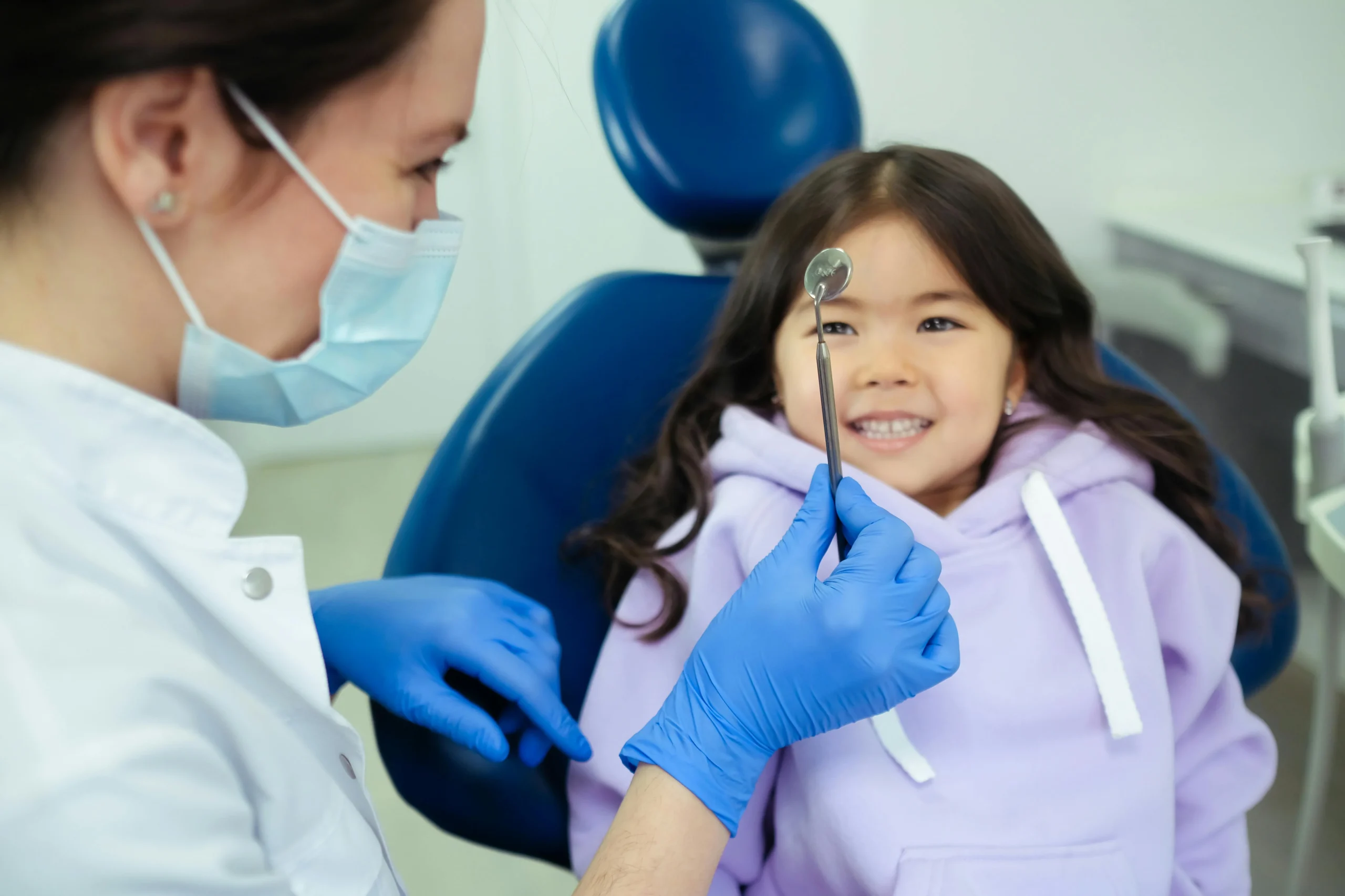 A photo of a smiling child in a dental chair with a pediatric dentist in a kid-friendly office.