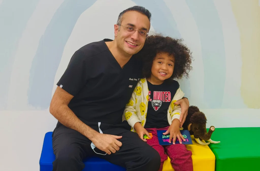 A photo of a pediatric dentist sitting beside a young child, creating a friendly and comfortable environment during a dental visit