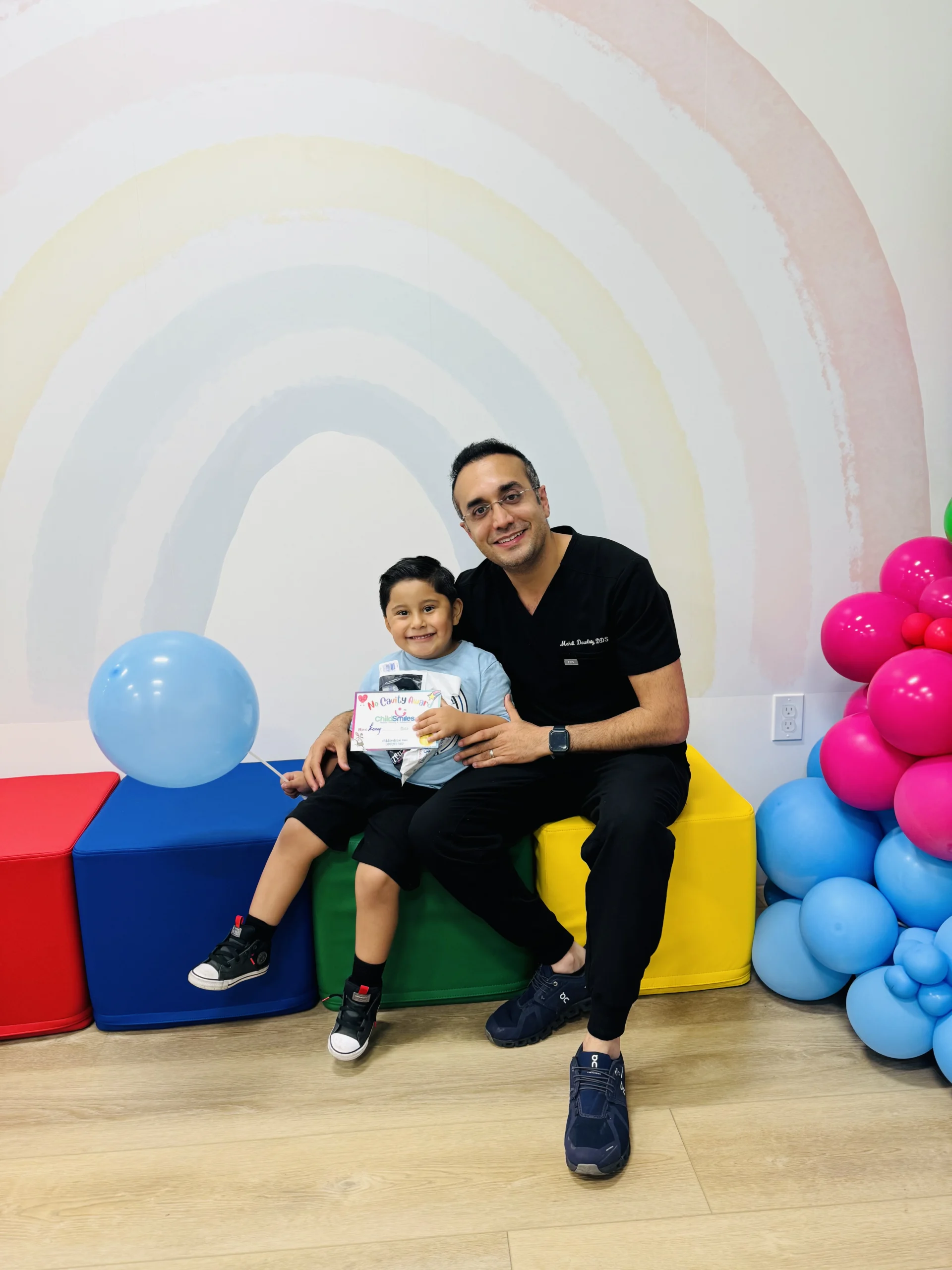 photo of a dentist sitting on colorful blocks with a child smiling while holding a no cavity award certificate