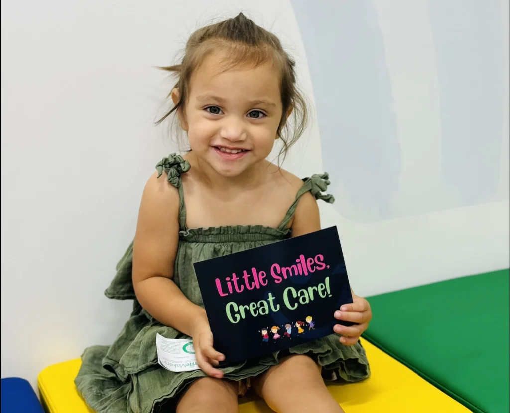photo of a girl smiling while holding a sign that says little smiles great care